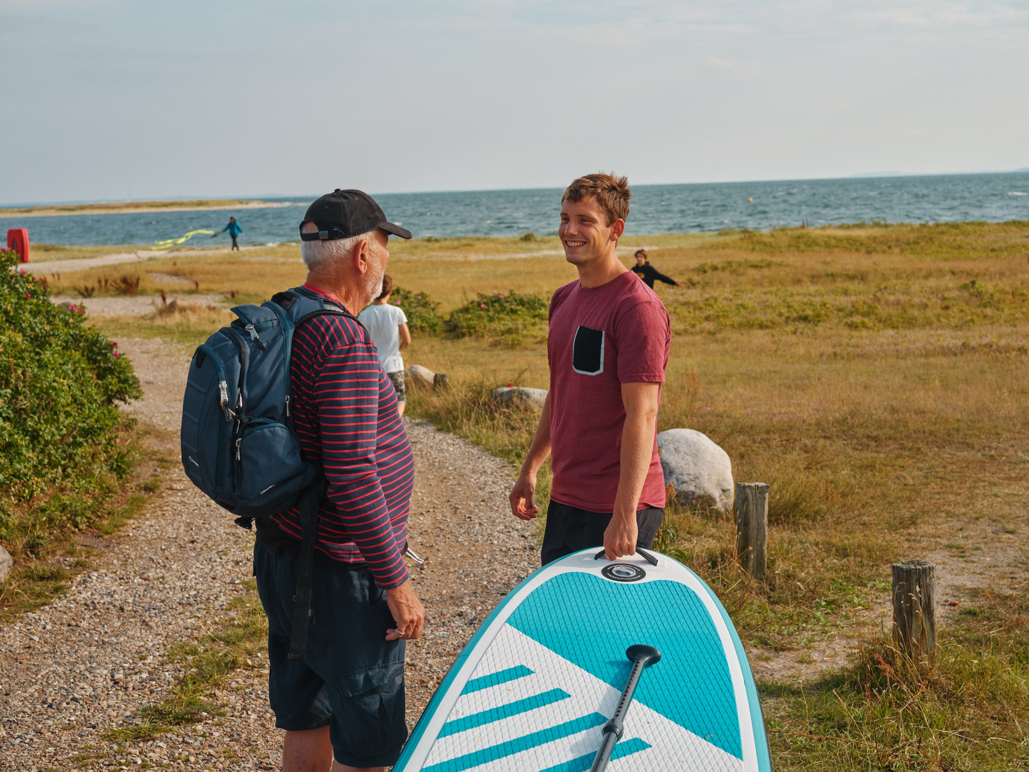 Pensioneret bedstefar og barnebarn med surfbræt og rygsæk ved strand